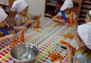 Dziewczynki przy stole obierają marchewki.